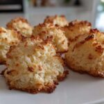 A close-up of several golden brown, freshly baked Low Carb Coconut Cookies arranged on a white plate.