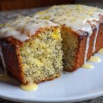A slice cut from a Moist Lemon Poppy Seed Loaf, topped with dripping zesty glaze and poppy seeds.