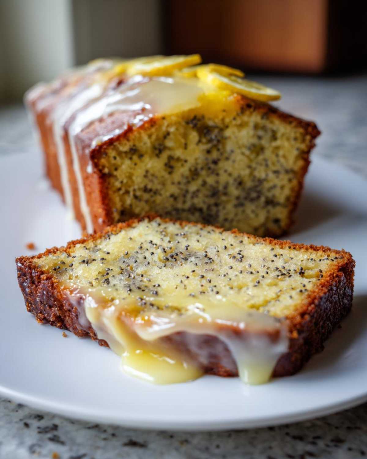 A slice of Moist Lemon Poppy Seed Loaf covered in dripping zesty glaze, with the rest of the loaf behind it.