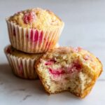 Close-up of Moist Sour Cream Rhubarb Muffins, one is bitten into revealing the tender interior and pink rhubarb pieces.
