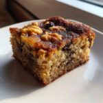 A moist, caramelized square of Ooey Gooey Banana Bars Dessert topped with walnuts, served on a white plate.