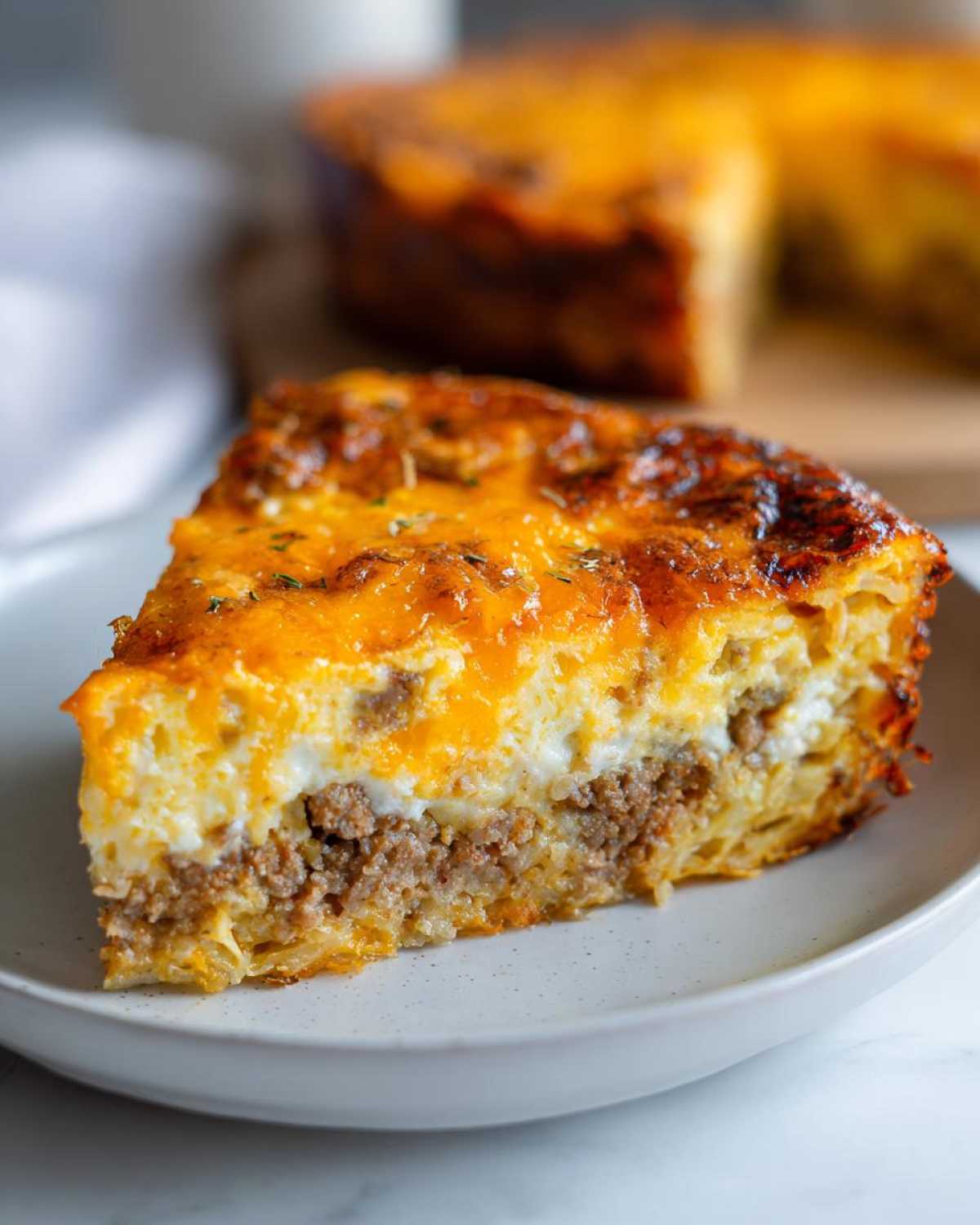 A thick slice of layered Breakfast Casserole featuring a hash brown base, sausage, egg, and melted cheddar cheese topping.